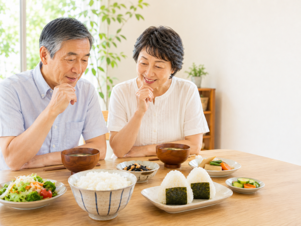 温かいごはんとおにぎりを前に食事について話しているシニア夫婦のイメージ画像