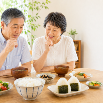 温かいごはんとおにぎりを前に食事について話しているシニア夫婦のイメージ画像