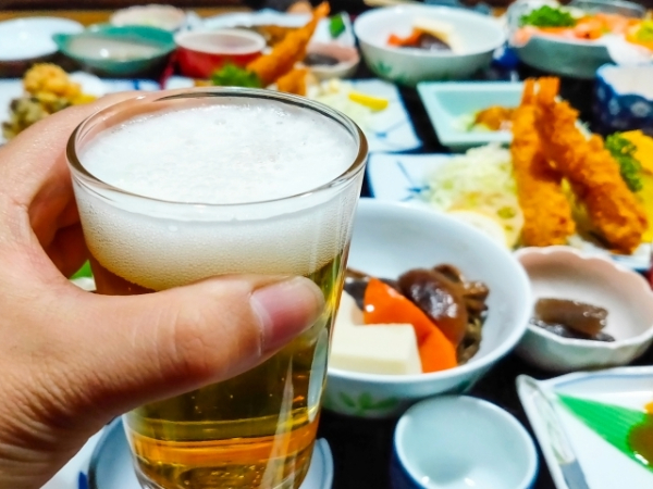 美味しそうな食事を目の前に、ビールで乾杯するイメージ画像