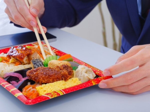 添加物の多そうなお弁当を食べる男性のイメージ画像