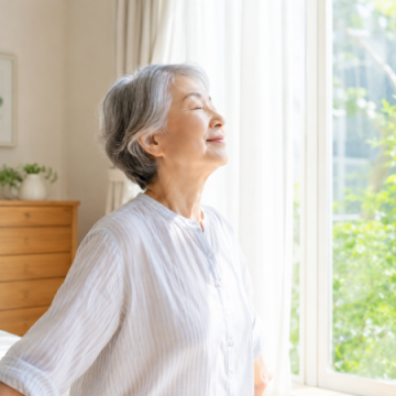 朝窓辺で深呼吸をしているシニア女性のイメージ画像