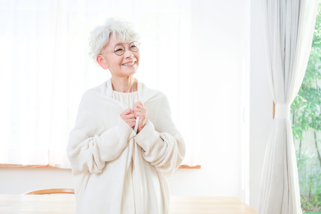 窓辺でほほ笑むシニア女性のイメージ画像