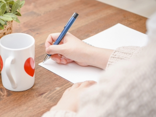 ノートにメモをする女性の手元のイメージ画像