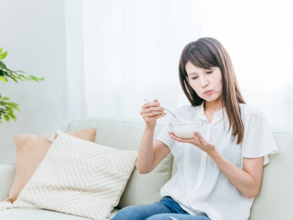 ヨーグルトを前に少し考えている女性のイメージ画像
